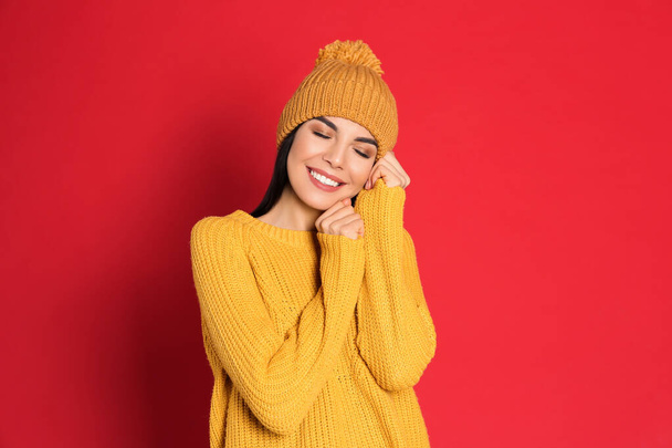 Junge Frau mit warmem Pullover und Hut auf rotem Hintergrund. Wintersaison - Foto, Bild