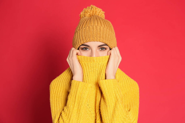 Young woman wearing warm sweater and hat on red background. Winter season - Φωτογραφία, εικόνα