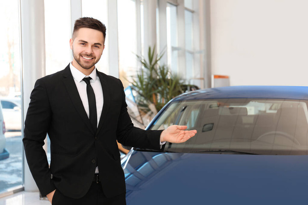 Young salesman near new car in dealership - Фото, зображення