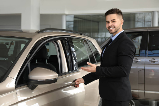 Young salesman near new car in dealership - Zdjęcie, obraz