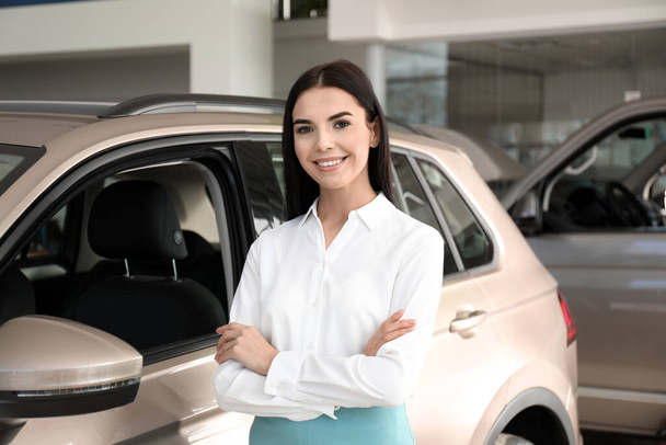 Young saleswoman near new car in dealership - Фото, изображение