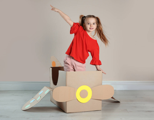 Cute little child playing with cardboard plane near beige wall - Foto, immagini
