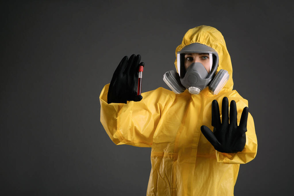 Woman in chemical protective suit holding test tube of blood sample on grey background. Virus research - Fotó, kép