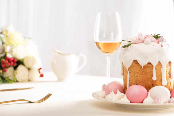 valikoiva painopiste herkullinen pääsiäiskakku koristeltu marenki vaaleanpunainen ja valkoinen munat lautasella lähellä viinilasia ja kukkia
 - Valokuva, kuva