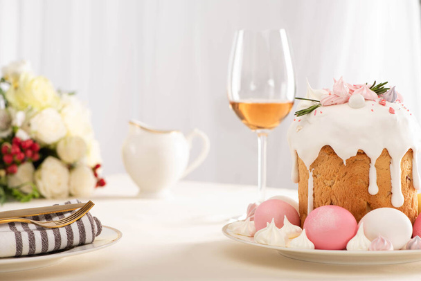 selective focus of delicious Easter cake decorated with meringue with pink and white eggs on plate near wine glass and flowers - Photo, Image