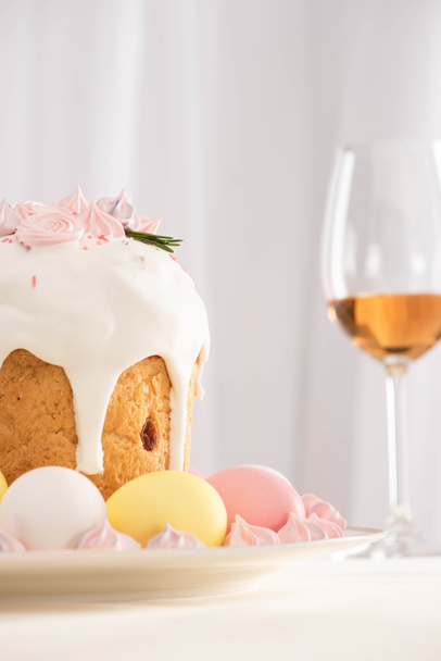 selective focus of Easter cake decorated with meringue near colorful eggs on plate and wine glass - Fotoğraf, Görsel