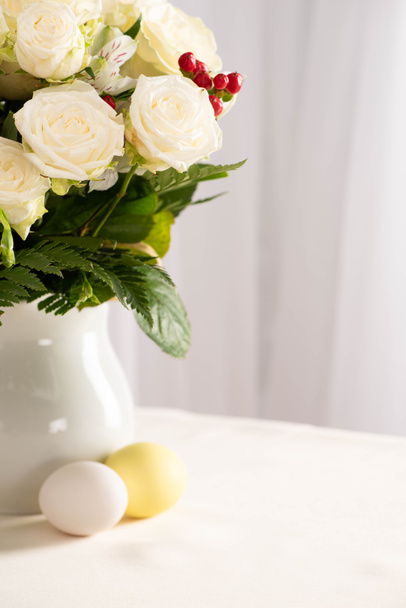 Vase mit frischen Blumen auf dem Tisch neben bunten Ostereiern - Foto, Bild