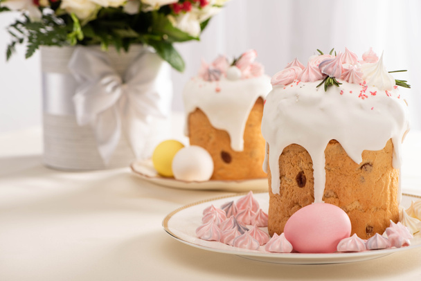 selective focus of festive Easter cake decorated with meringue near painted eggs on plates and flowers - Foto, afbeelding