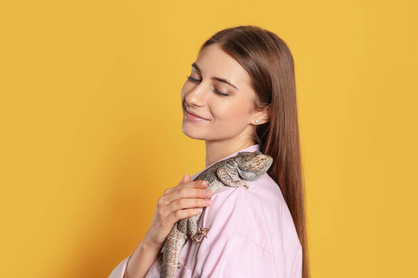 Woman holding bearded lizard on yellow background. Exotic pet - Photo, Image