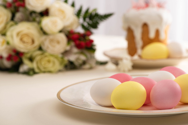 selective focus of painted eggs on plate near delicious Easter cake and flowers - Фото, изображение
