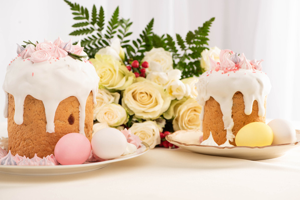 delicious Easter cakes decorated with meringue with colorful eggs on plate near flowers - 写真・画像