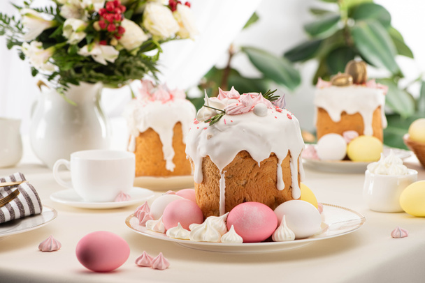 selective focus of Easter cakes with colorful eggs near flowers in vase on table - Photo, image