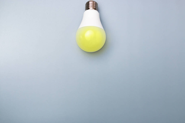 switched on led bulb with yellow light on grey background with copy space for advert. business idea concept. - Photo, Image