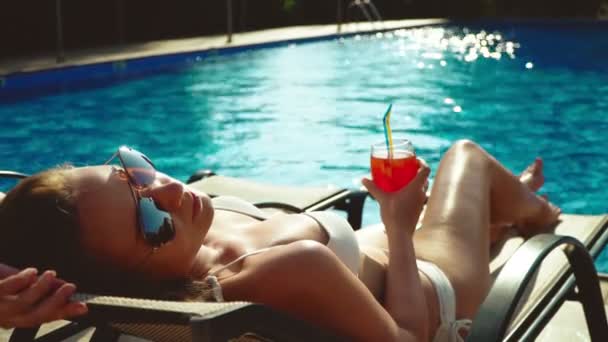 Nainen cocktailin kanssa makaa uima-altaan lähellä
. - Materiaali, video