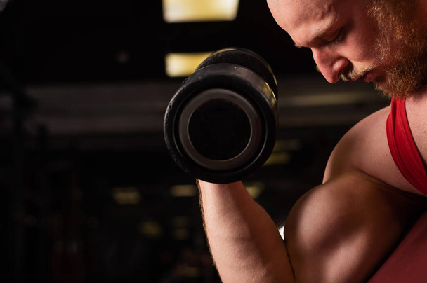 Bald man doing biceps exercise in the gym. Muscular man is engaged in bodybuilding. Close-up of male hands. - Foto, Bild