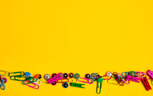Office supplies in the form of colored buttons and paper clips on the edges of the photo on yellow background, copy space, border and frame - Foto, Imagen