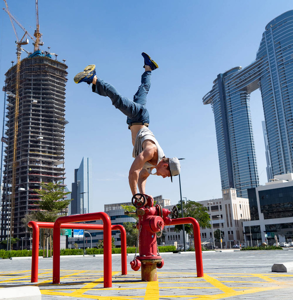 Flexible Acrobat keep balance with one hand on the fireman hydrant with blurred Dubai cityscape. Concept of modern and safety  - Photo, Image