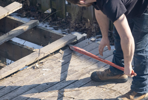 Hombre desmantelando una cubierta de madera vieja con una barra roja en un patio trasero
 - Foto, Imagen