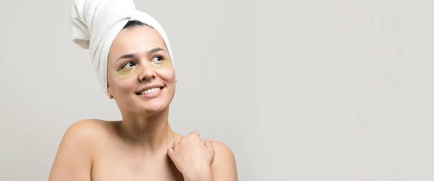Young beautiful girl in a white towel on his head wears collagen gel patches under her eyes. Mask under eyes treatment face. - Photo, Image
