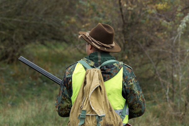 Período de caza, temporada de otoño abierta. Un cazador con un arma en sus manos en ropa de caza en el bosque de otoño en busca de un trofeo. Un hombre está con armas y perros de caza rastreando el juego. - Foto, Imagen
