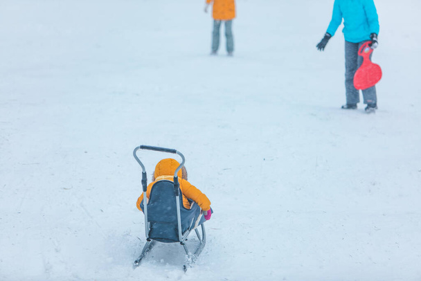 Маленький ребенок на санях скользит вниз по зимнему снежному холму - Фото, изображение