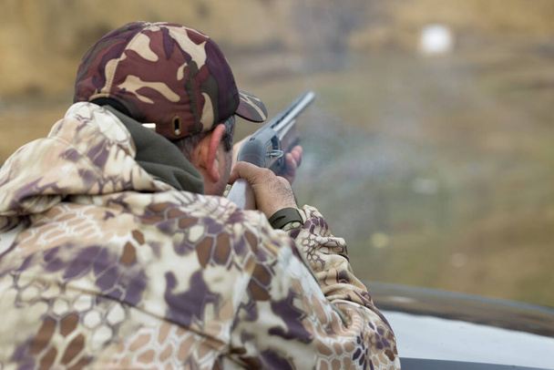 Um caçador camuflado no campo de tiro calibra a arma. Um homem dispara contra alvos.
. - Foto, Imagem