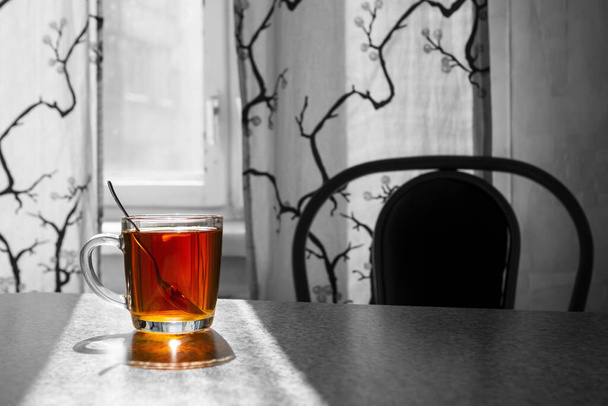 Κύπελλο με πολύχρωμο τσάι σε άχρωμο φόντο του τραπεζιού και κουρτίνες στο παράθυρο - Φωτογραφία, εικόνα