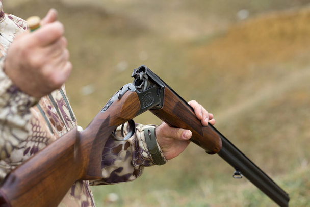 Laadt een jachtgeweer, jaagt op een fazant met honden. Een jager in camouflage staat met een wapen.. - Foto, afbeelding
