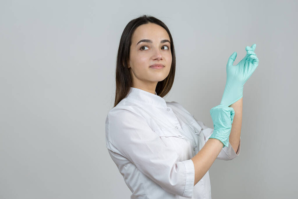 Ένα κορίτσι γιατρός σε γάντια λάτεξ και ένα λευκό παλτό ετοιμάζεται για τις διαδικασίες. - Φωτογραφία, εικόνα