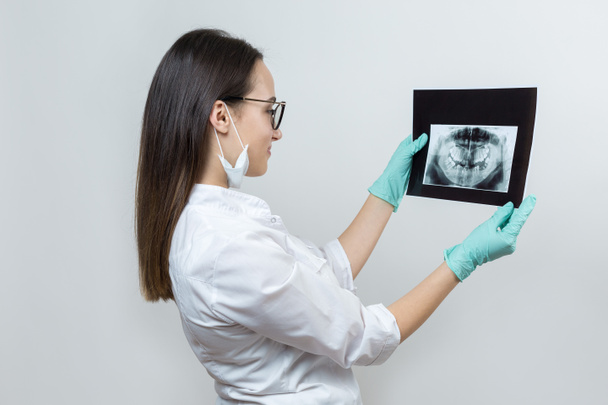 Dívka zubař v bílém plášti drží snímek pacientových zubů. - Fotografie, Obrázek