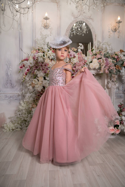 Little girl lady in pink dress and hat sits among magic flowers - Photo, image