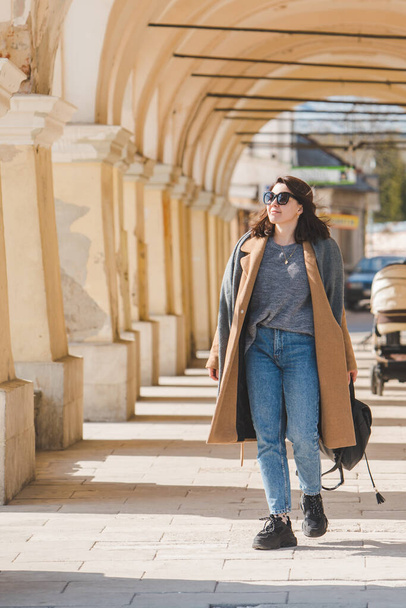 młoda dość modna kobieta spaceruje w brązowym płaszczu przez ulicę miasta - Zdjęcie, obraz