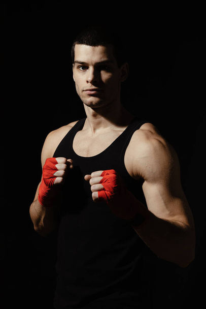 Boxe retrato masculino de pé em um rack sobre fundo preto com ligaduras vermelhas em suas mãos. Luz e sombras jogar
. - Foto, Imagem