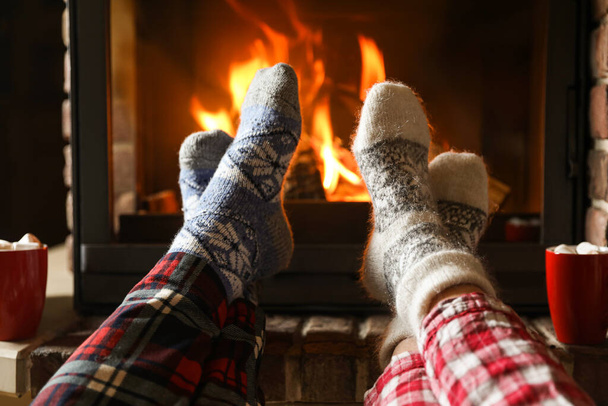 Couple in pajamas resting near fireplace indoors, closeup. Winter vacation - Foto, Imagen