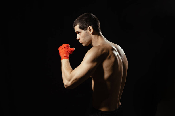 Sportsman boxer practicing side kick. Red bandages on the hands. Muscular boxer on black background. Sport concept. - Photo, image