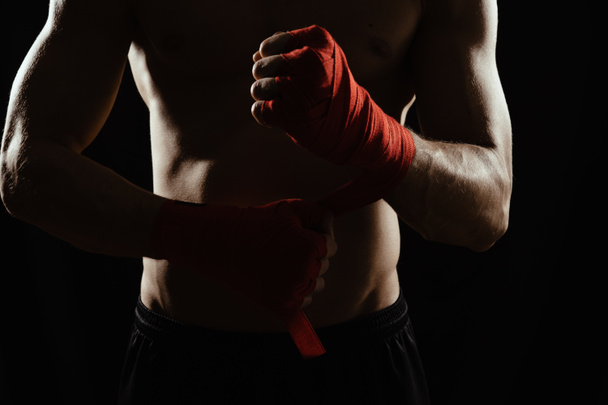 Közelkép egy fiatal bokszoló kezéről, aki piros kötést húz fel meccs, harc vagy edzés előtt. - Fotó, kép