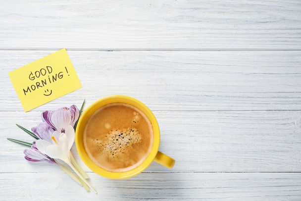 Delicious coffee, flowers and card with GOOD MORNING wish on white wooden table, flat lay. Space for text - Foto, Imagen