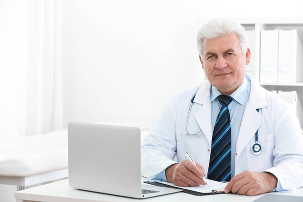 Portrait of senior doctor in white coat at workplace - Photo, Image