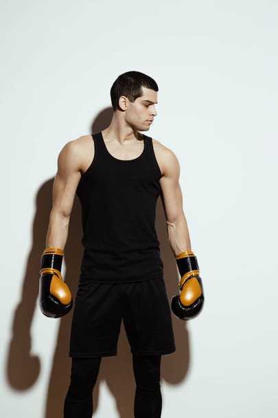 Wysocy, atrakcyjni sportowcy, w czarnej koszulce sportowej i spodenkach, z silnymi ramionami pozującymi w rękawiczkach bokserskich na białym tle - Zdjęcie, obraz