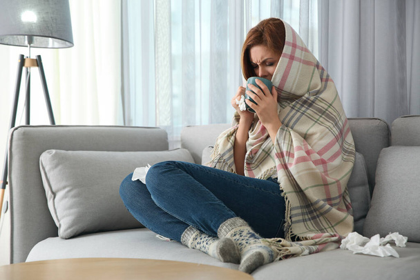Sick woman wrapped in plaid with cup of hot drink at home. Influenza virus - Φωτογραφία, εικόνα