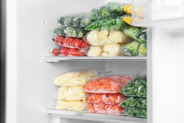 Plastic bags with different frozen vegetables in refrigerator - Фото, изображение