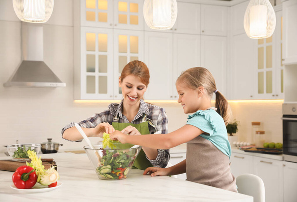 Mother and daughter cooking salad together in kitchen - Photo, image