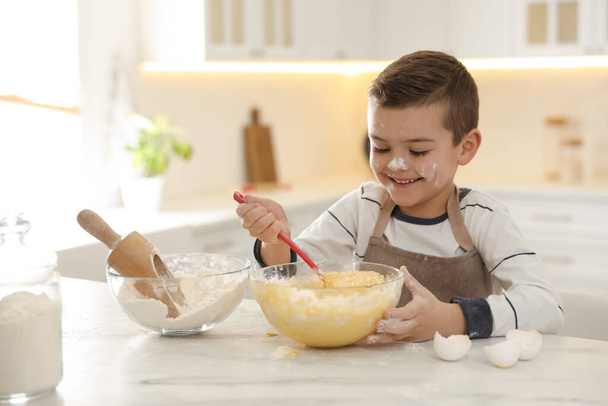 Cute little boy cooking dough at table in kitchen - Fotó, kép