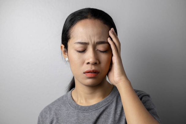 Mujer joven con estrés y dolores de cabeza sobre un fondo gris. Mujer asiática con dolor de cabeza. Mujeres con mucho estrés
. - Foto, Imagen