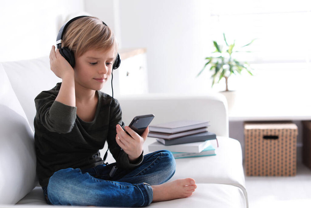 Cute little boy with headphones and smartphone listening to audiobook at home - Φωτογραφία, εικόνα