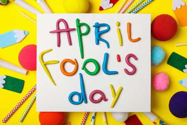 Paper note with phrase APRIL FOOL'S DAY and decor on yellow background, flat lay - Foto, Imagem