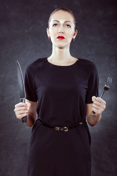 Egy gyönyörű fiatal nő portréja fekete háttérrel, késsel és villával a kezében.. - Fotó, kép