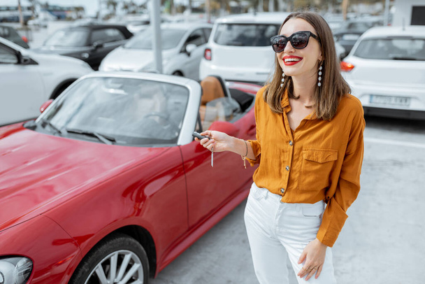 Mujer feliz con llaves cerca del coche en el aparcamiento
 - Foto, imagen