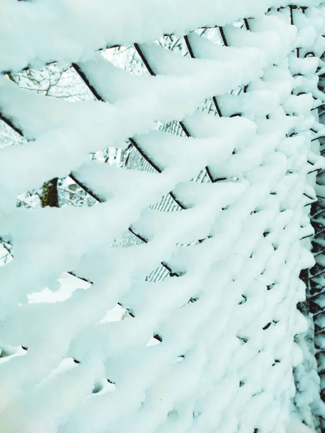 Iron net fence covered snow. Metal rusty fence-mesh netting in the snow. Close-up shot of snow on a fence. Lattice fence covered with fresh snow. White background texture. Winter background. - 写真・画像