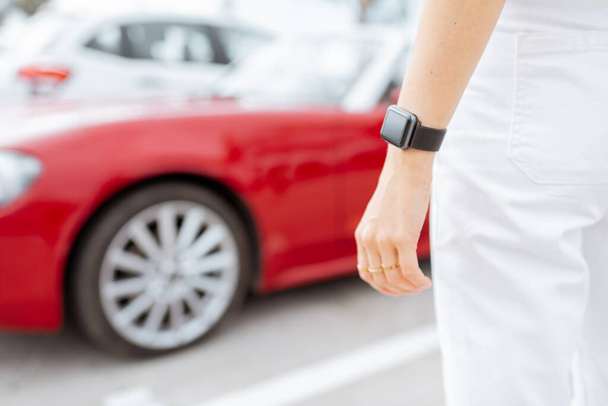 Розумний годинник на жіночому зап'ясті з машиною на фоні, крупним планом
 - Фото, зображення